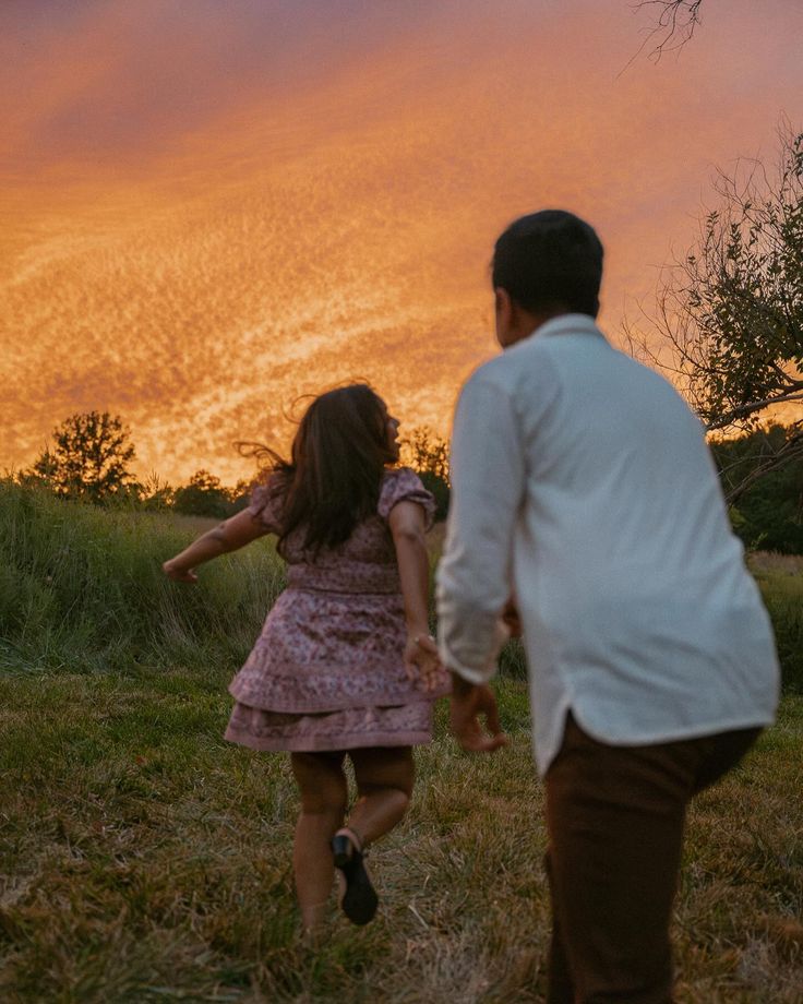 a man and woman walking through a field at sunset