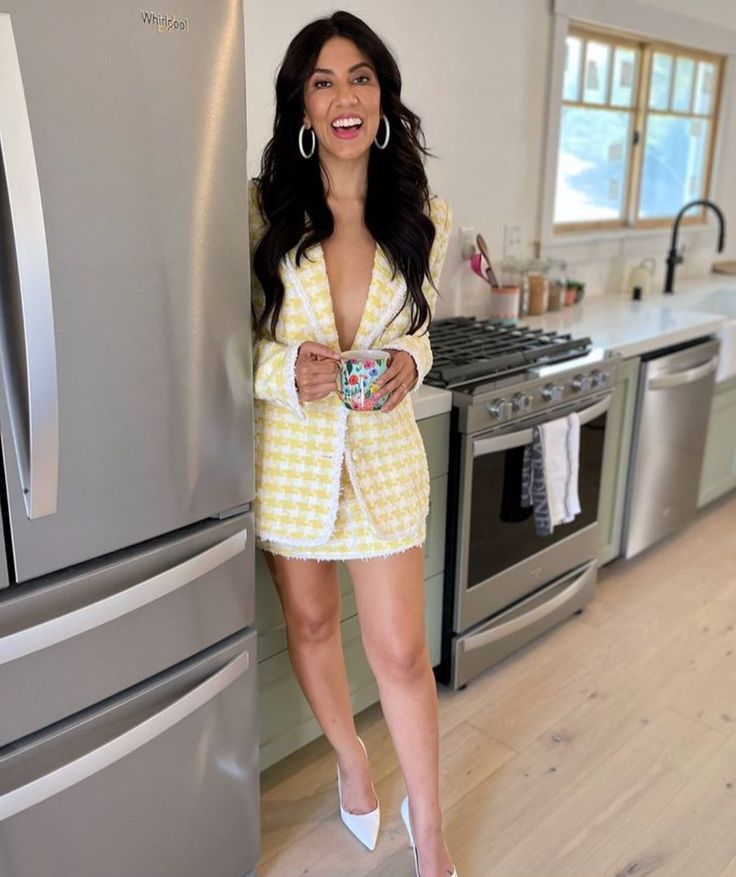 a woman in a yellow and white suit standing next to a silver refrigerator freezer