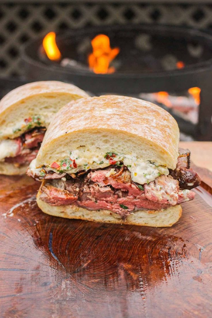 two sandwiches sitting on top of a cutting board next to an open fire pit in the background