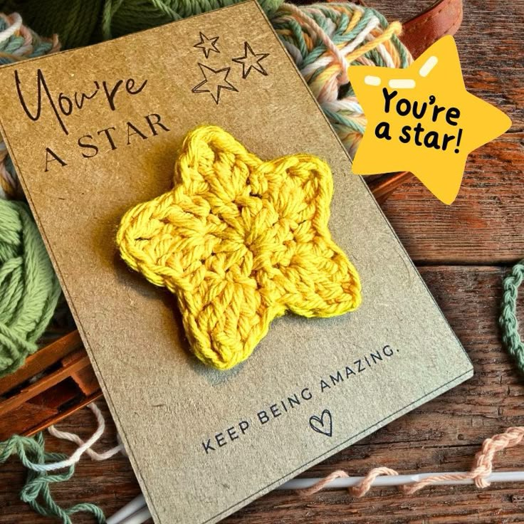 a yellow crochet star brooch sitting on top of a book next to yarn