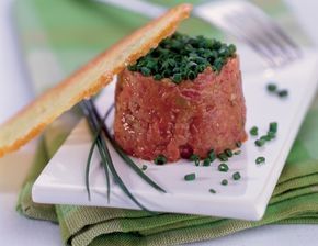 there is a small piece of meat on a white plate with green garnish