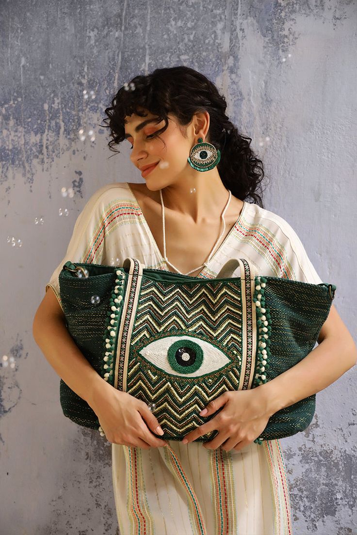 Keeping up with the trendiest color of the season, say hello to your favourite Evil Eye Embellished Tote, now here in an Evergreen Forest color. A show-stopping glory for when all eyes must be on you. This tote bag is perfect for everyday use and for special occasions too! It features a hand beaded evil eye in front for protection, and is hand-embellished with beads and sequins for a touch of glamour. The double shoulder straps are adorned with lace detail, and the bag has a magnetic button clos Green Bohemian Shoulder Bag For Shopping, Green Shoulder Bag For Shopping, Green Bohemian Shopping Bag, Green Embellished Rectangular Shoulder Bag, Embellished Green Rectangular Shoulder Bag, Green Large Capacity Party Bags, Green Summer Party Bags, Green Embroidered Bag For Everyday Use, Green Shoulder Bag For Summer Parties