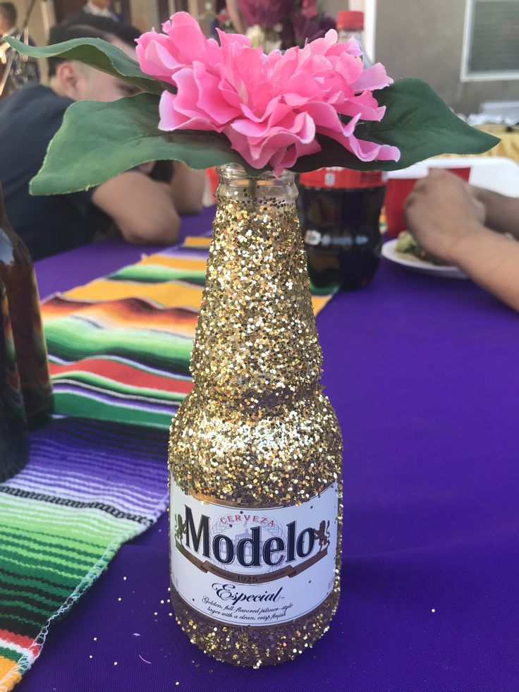 a pink flower sitting in a bottle on top of a purple table cloth next to other bottles