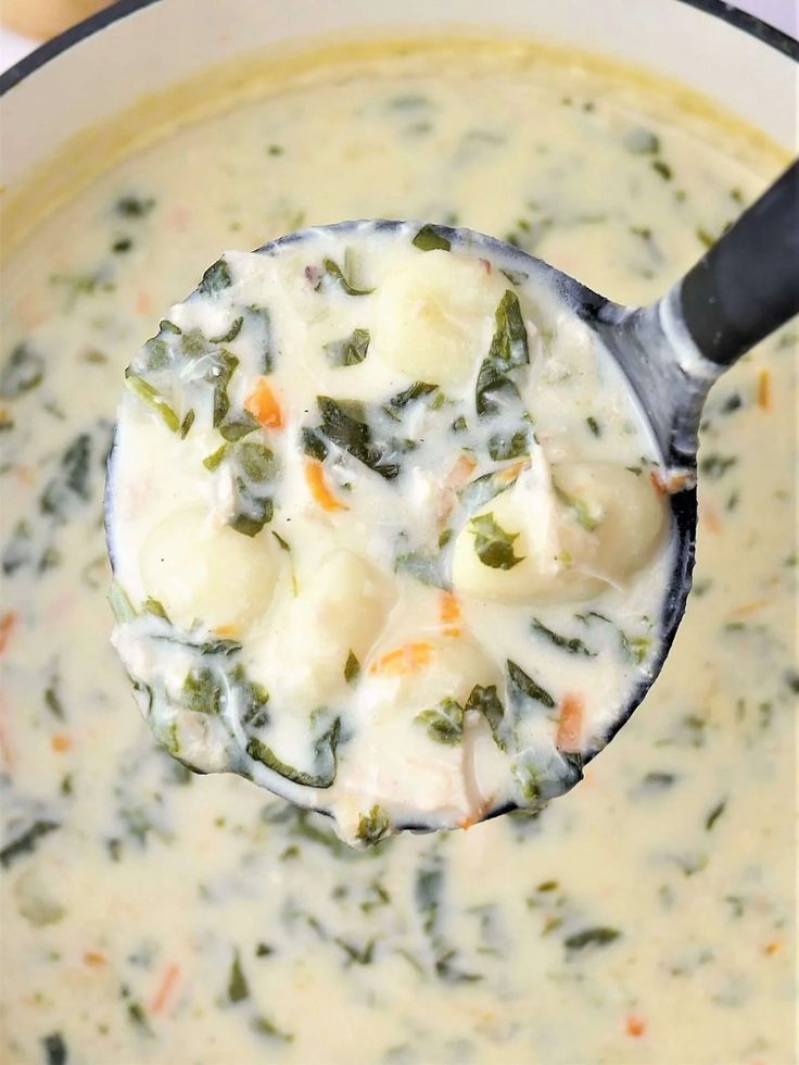 a ladle full of soup with broccoli and dumplings in it, ready to be eaten