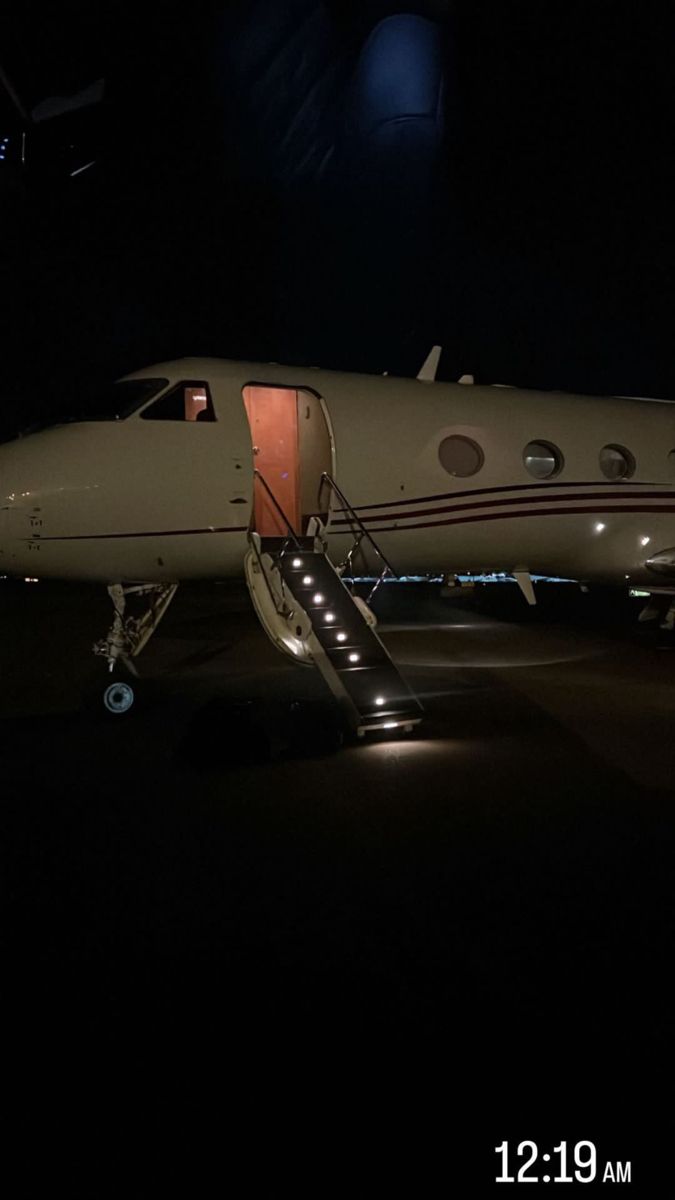 an airplane sitting on the tarmac at night with its door open and stairs down