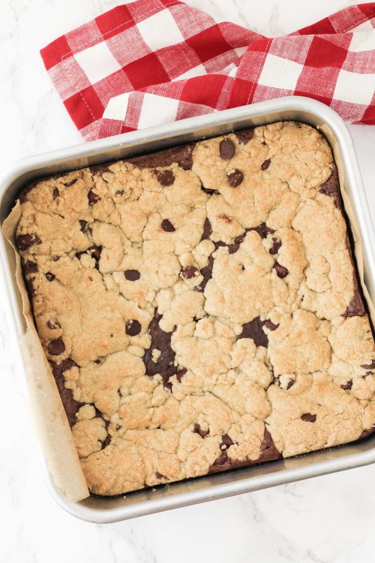 a pan filled with chocolate chip cookie bars on top of a white and red checkered table cloth