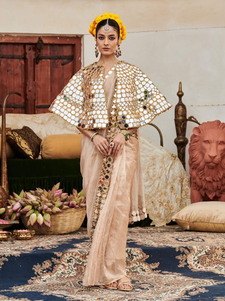 A sophisticated ensemble, this beige sari features a stunning mirror work border that adds an elegant touch. Styled with a full mirror work cape, this outfit beautifully merges traditional charm with modern glamour, making it a perfect choice for special occasions and celebrations. Cape Sleeves Anarkali Set With Cutdana For Eid, Festive Sharara With Cutdana And Cape Sleeves, Diwali Sharara With Cutdana And Cape Sleeves, Festive Traditional Wear With Cutdana And Cape Sleeves, Navratri Dupatta With Cutdana And Cape Sleeves, Diwali Cutdana Sharara With Cape Sleeves, Bollywood Style Choli With Cape Sleeves And Cutdana, Cape Sleeve Anarkali Set With Cutdana For Festive Occasions, Diwali Lehenga With Cape Sleeves And Cutdana