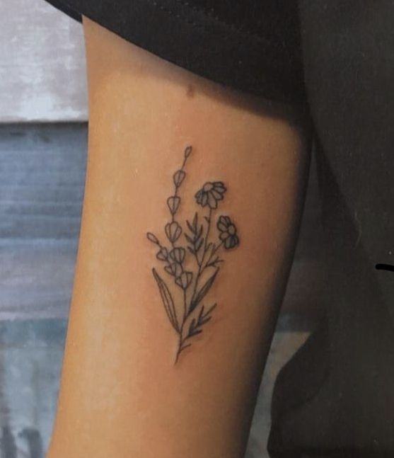 a small flower tattoo on the ankle is shown in black and grey colors, with tiny flowers coming out of it