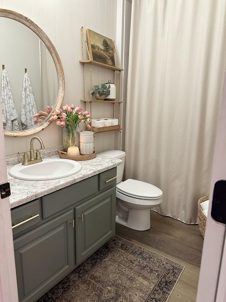 a white toilet sitting next to a bathroom sink under a round mirror on top of a wooden cabinet