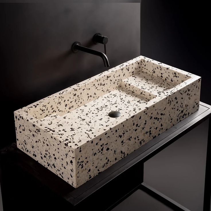 a bathroom sink with black and white speckles on the counter top in front of a dark wall