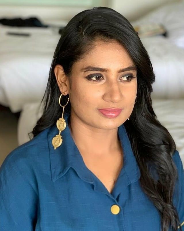 a woman with long black hair and blue shirt posing for a photo in front of a bed