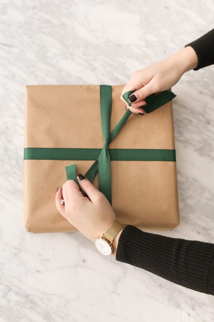 a woman holding a wrapped present on top of a white table with a green ribbon