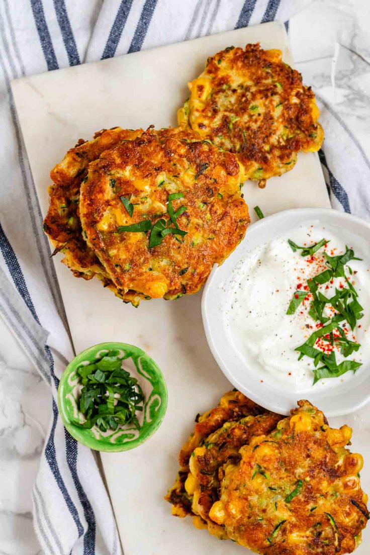 three crab cakes on a cutting board with sour cream and green garnishes