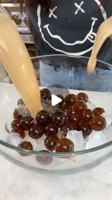 a person pouring some liquid into a glass bowl filled with jelly beans and ice cubes