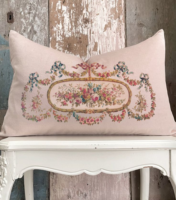 an embroidered pillow on top of a white bench