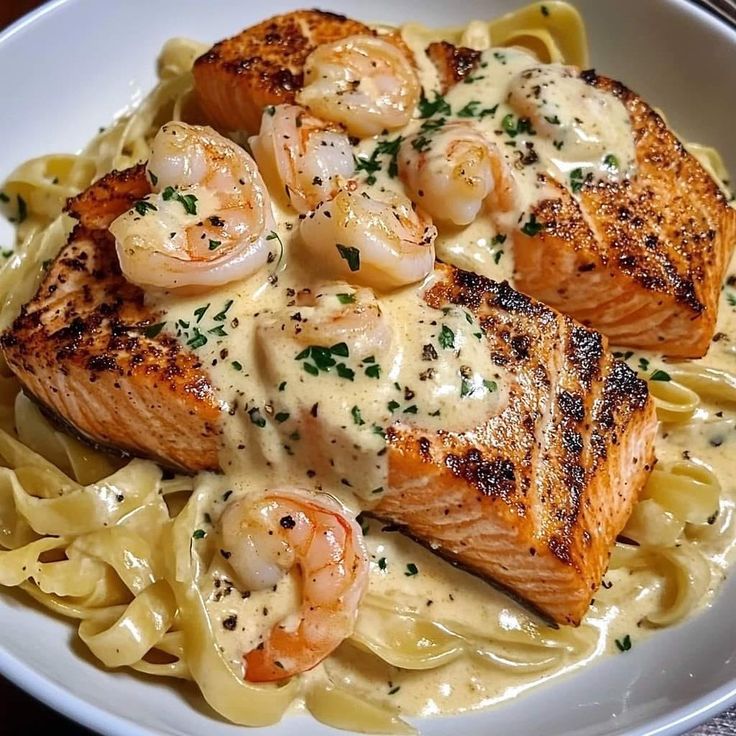 some salmon and shrimp are on top of pasta in a white bowl with lemon sauce