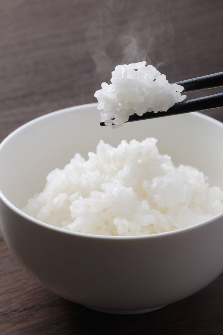 rice in a white bowl with chopsticks sticking out of it and steam rising from the top