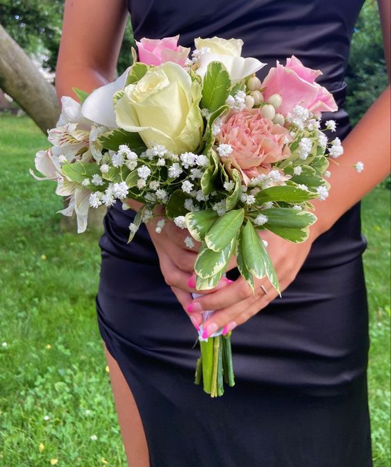 a woman in a dress holding a bouquet of flowers and greenery on the grass