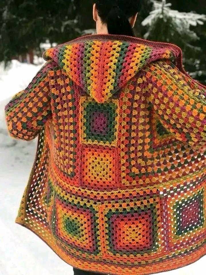 a woman wearing a colorful crocheted jacket in the snow with trees behind her