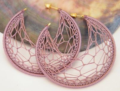 two pairs of pink lace hoop earrings on top of a table next to a painting