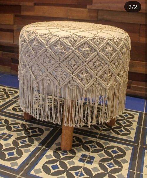 a white stool with tassels on it sitting on a tile floor next to a wall