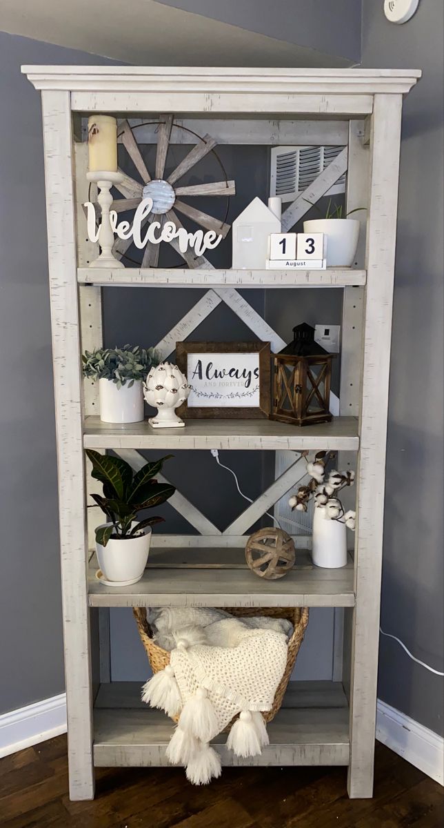 a white book shelf with some plants and other items on it in front of a gray wall