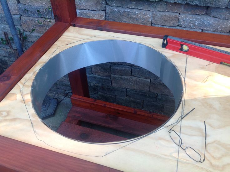 a circular mirror sitting on top of a wooden table next to a red tool and brick wall