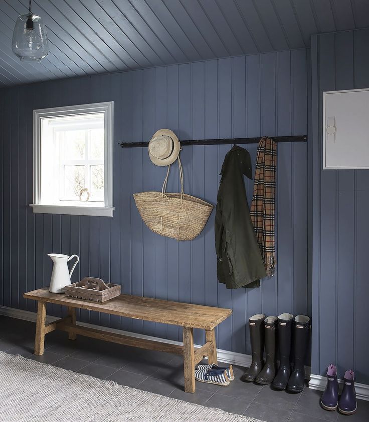 a wooden bench sitting under a window next to a coat rack and boot hanging on the wall