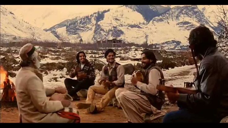 four people sitting around a campfire with mountains in the background and snow on the ground