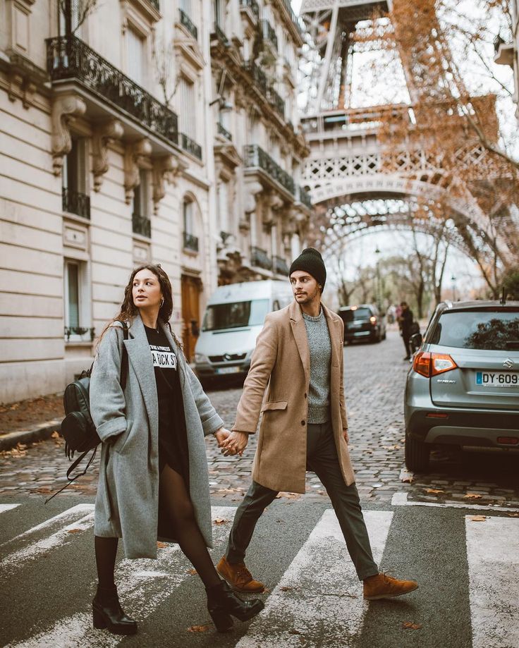 a man and woman crossing the street holding hands in front of the eiffel tower