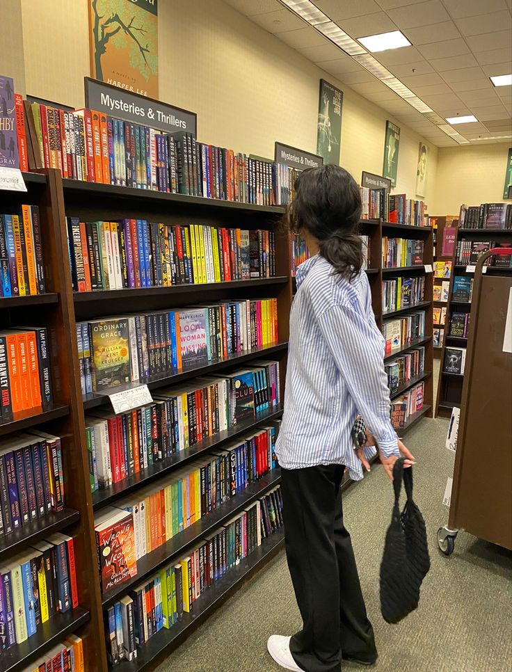 Woman standing in front of a shelf of books in a bookstore. She is turned away from the camera, scanning the book titles. Her hair is in a messy bun and she is wearing an oversized blue button down and black trousers. Bookstore Outfit, Bookstore Aesthetic, Instagram Feed Goals, Feed Goals, Coastal Granddaughter, Casual Summer Outfit, Outfit Style, Photo Inspo, Summer Outfit