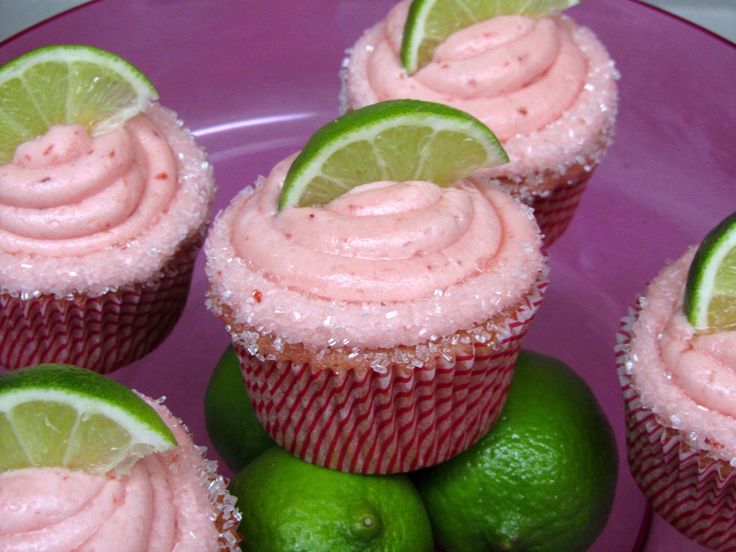 cupcakes with pink frosting and limes on a purple plate next to two limes