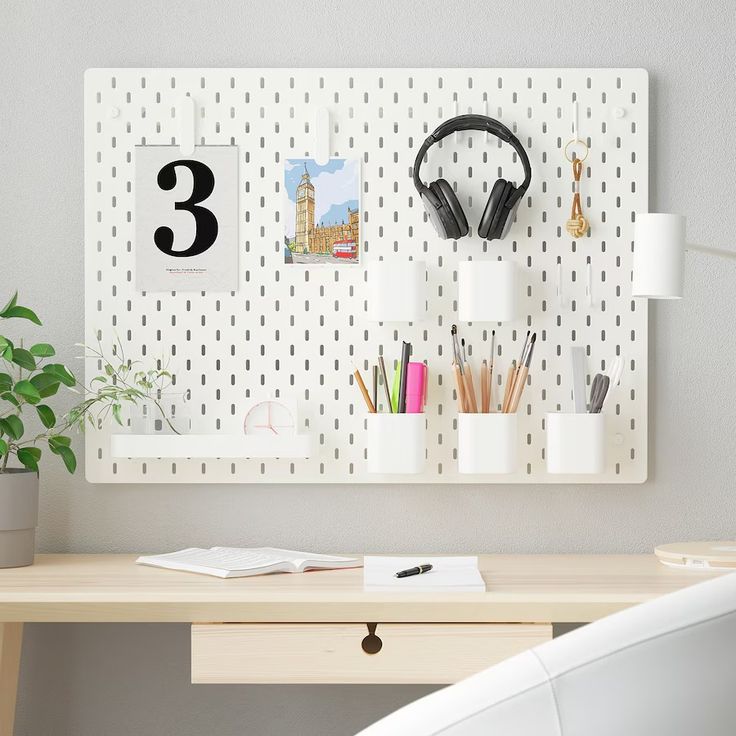 a desk with headphones on it next to a wall mounted calendar and pen holder