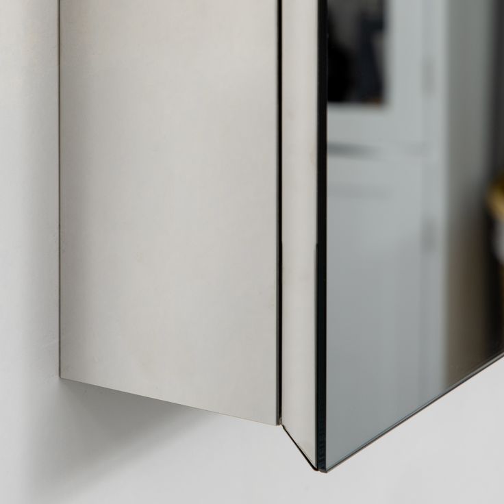 a mirror mounted to the side of a wall next to a white cabinet and door