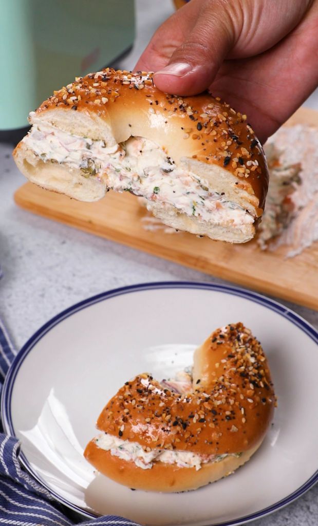 a person is taking a bite out of a bagel with cream cheese and sprinkles