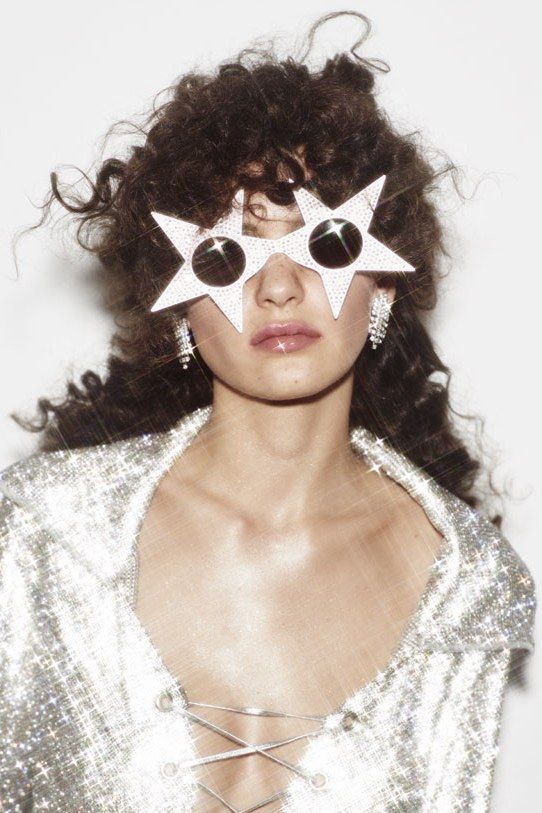 a woman with stars on her face and silver shirt over her eyes, standing in front of a white wall