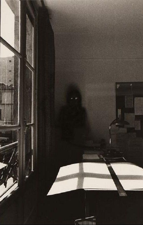 a black and white photo of a person sitting at a table in front of a window