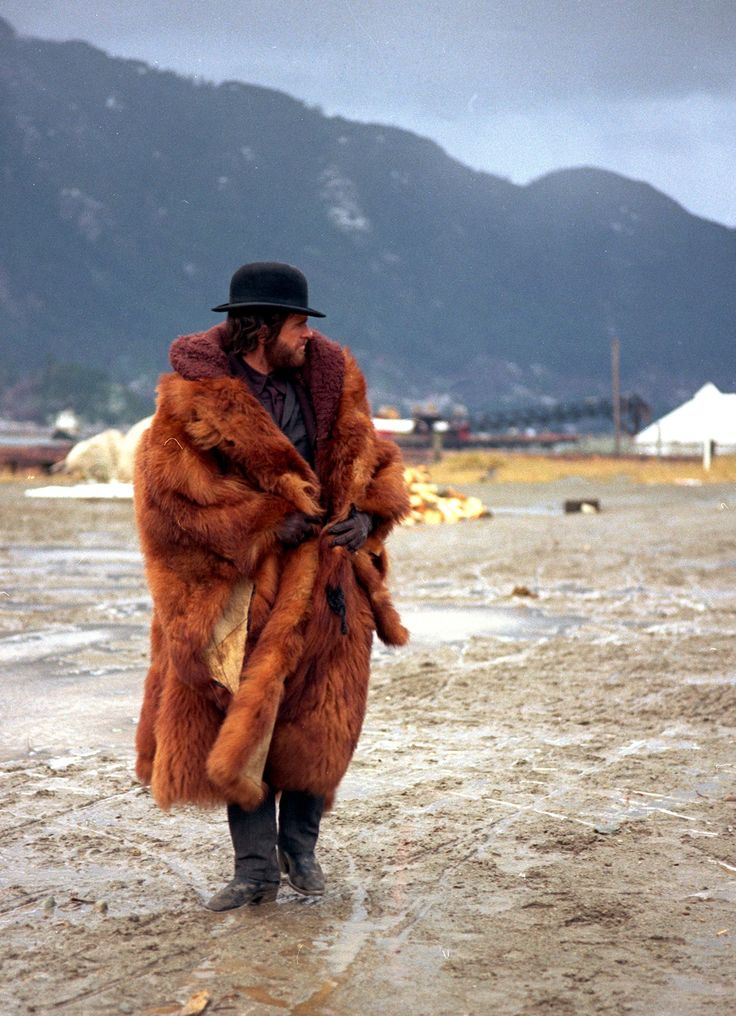 a man in a fur coat and hat walks through the mud