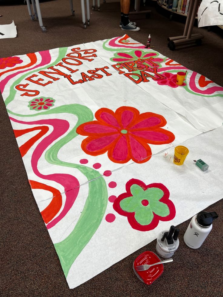 a large white blanket with flowers and words on it sitting on the floor next to paint cans