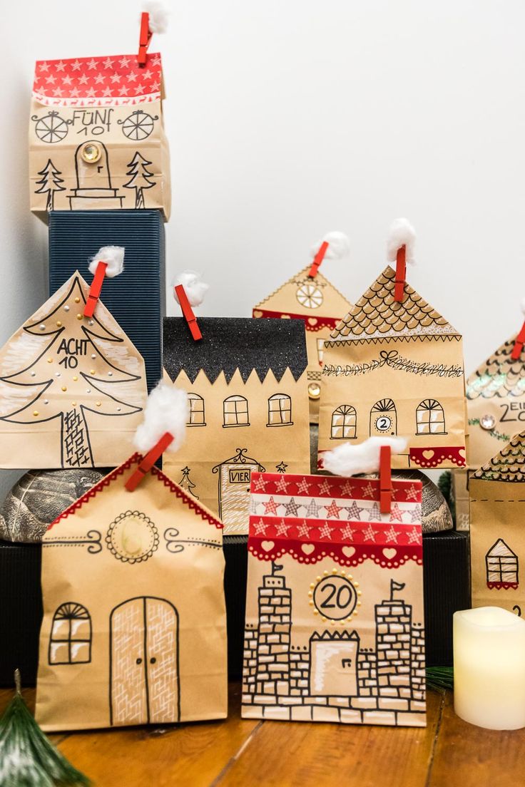 small paper bags with houses on them sitting on a wooden table next to a candle