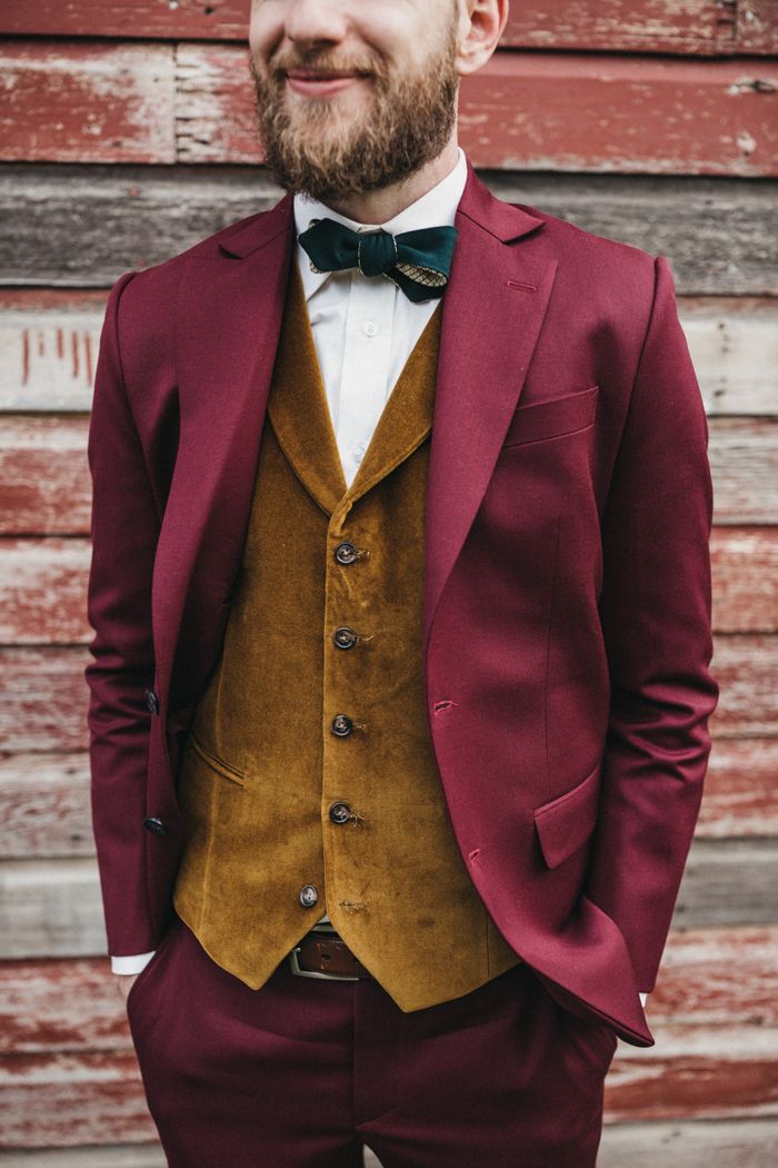 a man wearing a red suit and bow tie standing in front of a wooden wall