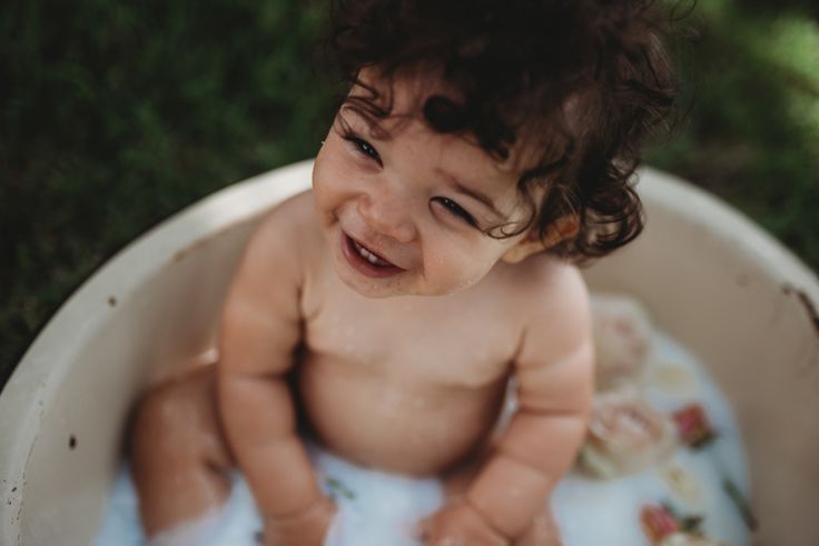 a smiling baby sitting in a bathtub on the grass and looking at the camera