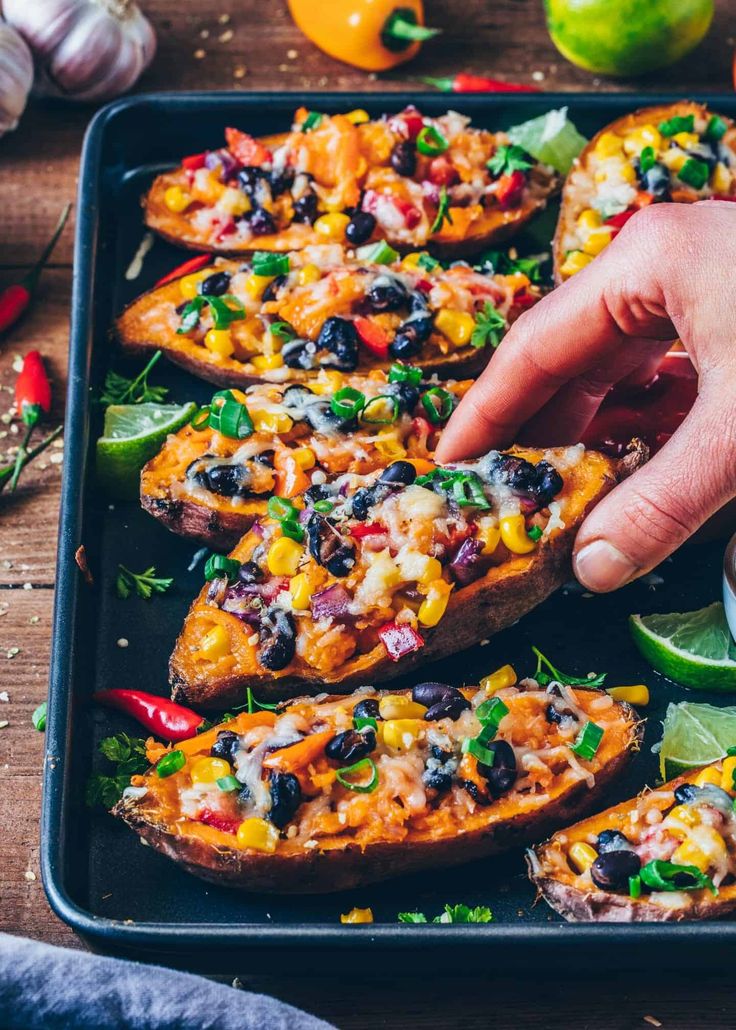 a person reaching for an enchilada on top of a baking sheet with limes