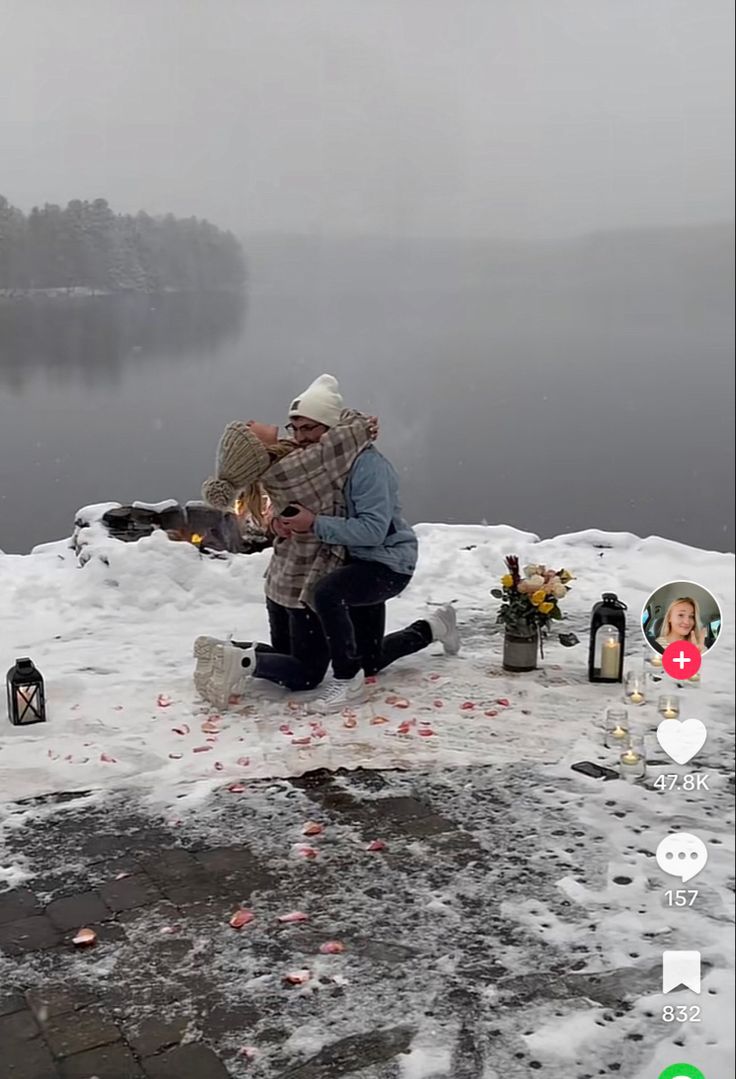 two people are sitting on the snow near some bottles and candles in front of a lake