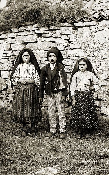 three children standing next to each other in front of a stone wall