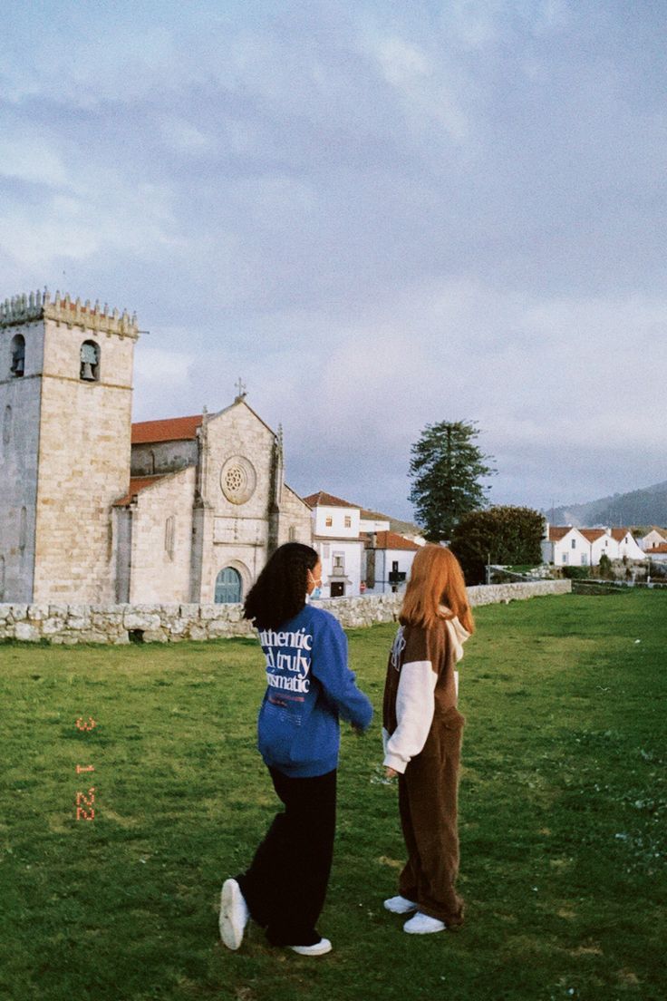 two women standing in the grass near a church