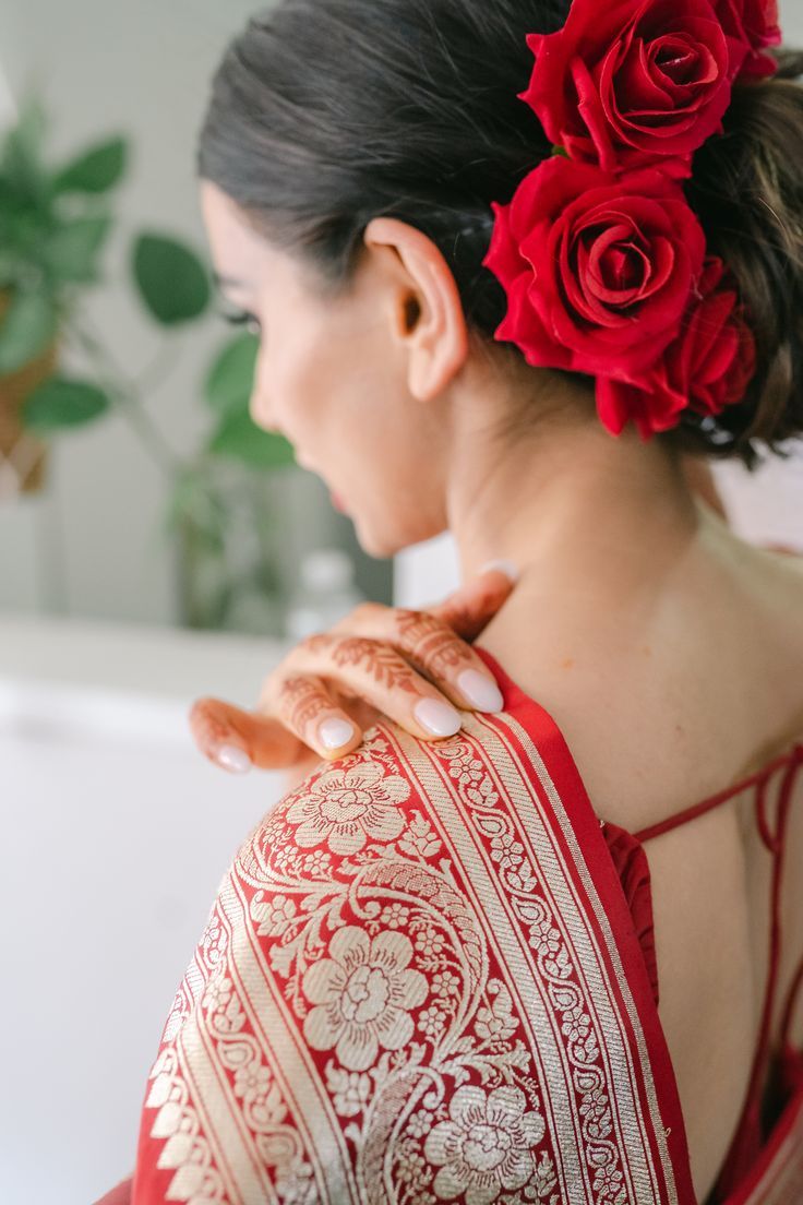 a woman wearing a red and white sari with flowers in her hair, looking off to the side