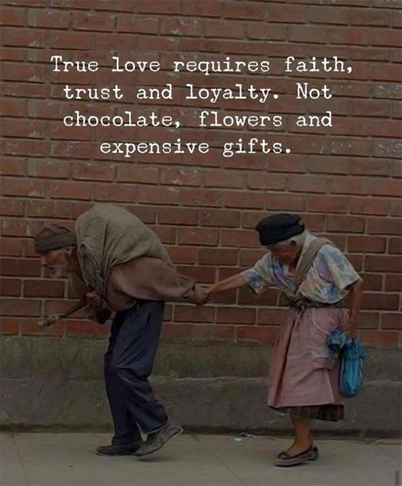 two people standing next to each other in front of a brick wall with words written on it