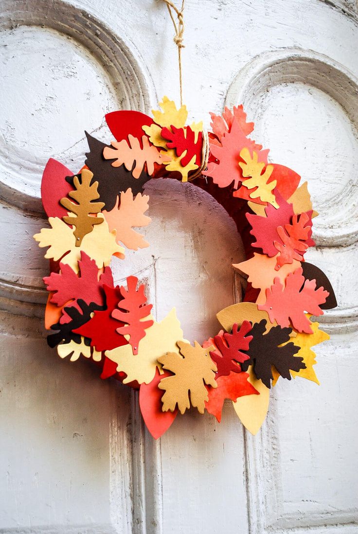 a wreath made out of paper leaves hanging on the front door with an ornament