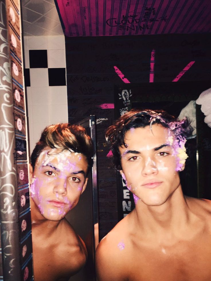 two men with face paint on their faces in front of a mirror, one is looking at the camera